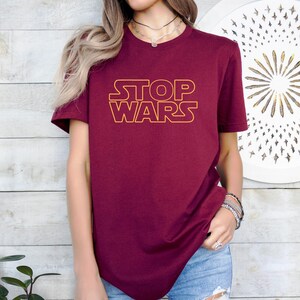 a woman wearing a red shirt with the word stop wars on it