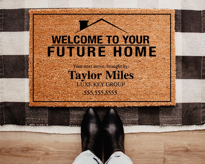 May include: A rectangular doormat with the text "WELCOME TO YOUR FUTURE HOME" in black. The mat is brown with a black border and sits on a black and white checkered rug. The text "Taylor Miles" and a phone number are also visible.