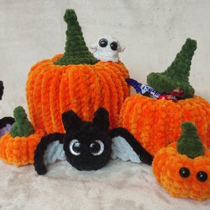 May include: A set of crocheted Halloween decorations, including pumpkins, a bat, a ghost, and a witch's hat. The pumpkins are orange and green, and the bat is black with purple wings. The ghost is white with googly eyes, and the witch's hat is green with a white brim.