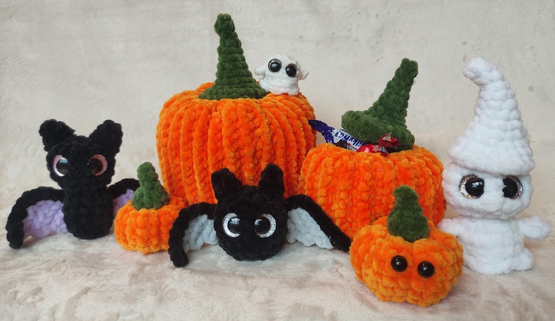 May include: A set of crocheted Halloween decorations, including pumpkins, a bat, a ghost, and a witch's hat. The pumpkins are orange and green, and the bat is black with purple wings. The ghost is white with googly eyes, and the witch's hat is green with a white brim.