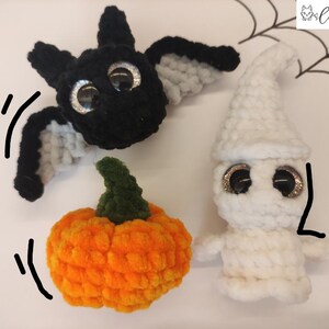 May include: Three crocheted Halloween decorations: a black bat with white wings, a white ghost with googly eyes, and an orange pumpkin with a green stem.