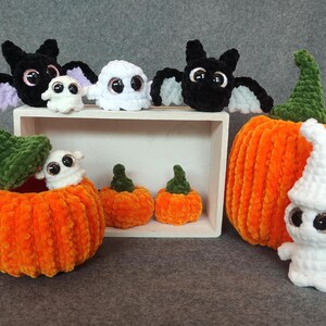May include: A set of crocheted Halloween decorations, including a black bat, white ghosts, and orange pumpkins. The pumpkins are decorated with green yarn and have a white ghost sitting on top of one.