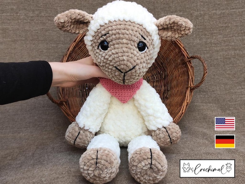May include: A crocheted plush lamb toy with a white body, brown face, and pink scarf. The lamb is sitting in a wicker basket.