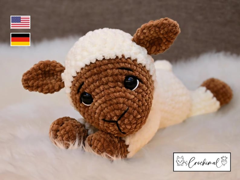 May include: A brown and white crocheted lamb toy with black eyes. The lamb is lying on a white fluffy surface.