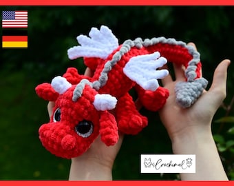 May include: A handmade crochet dragon plush toy featuring a vibrant red body, white wings, and white horns. The creature has large black eyes with silver glitter accents and a grey spine and tail tip. A small white label displays the text Crochimal.