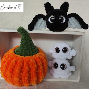 Könnte beinhalten: Ein gehäkelter Kürbis in orange und grün liegt in einer Holzkiste mit einer schwarzen gehäkelten Fledermaus und zwei weißen gehäkelten Geistern. Die Kiste trägt den Text "Crochimal" auf der Vorderseite.