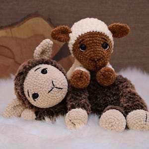 May include: Two crocheted sheep plushies, one brown and one white, with brown faces and black eyes. The sheep are lying on a white fluffy surface.