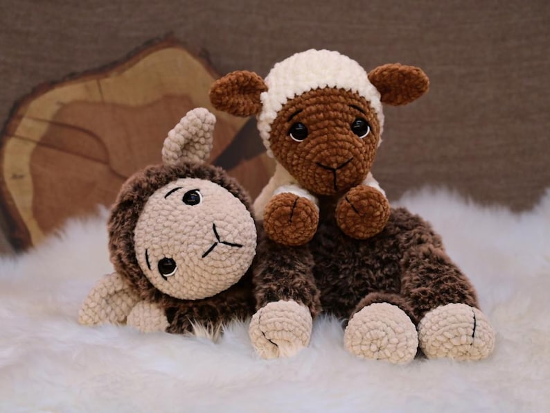 May include: Two crocheted sheep plushies, one brown and one white, with brown faces and black eyes. The sheep are lying on a white fluffy surface.
