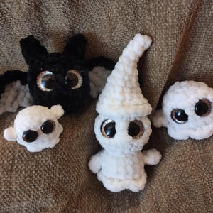 May include: Four crocheted plush toys, a black bat, a white ghost with a hat, and two smaller white ghosts. All the toys have large googly eyes.