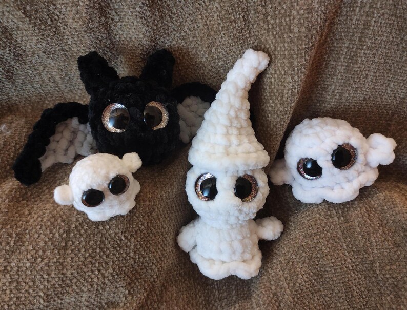 May include: Four crocheted plush toys, a black bat, a white ghost with a hat, and two smaller white ghosts. All the toys have large googly eyes.