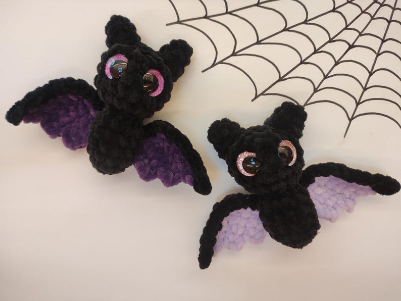 May include: Two black crocheted bats with purple wings and large pink eyes.