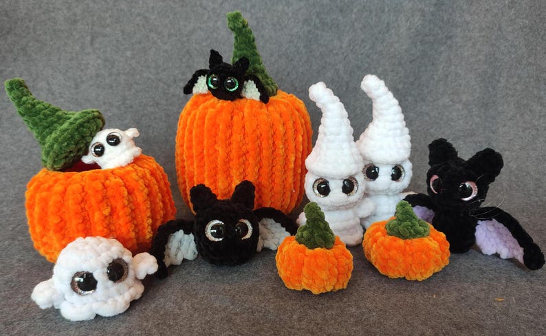 May include: A collection of crocheted Halloween decorations, including pumpkins, ghosts, and bats. The pumpkins are orange and have a fuzzy texture. The ghosts are white and have googly eyes. The bats are black with purple wings.