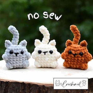 May include: Three crocheted cat toys in gray, white, and orange. The toys are sitting on a wooden surface. The text "no sew" is written above the toys.