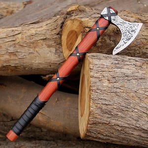 May include: A handcrafted axe with a wooden handle and a silver blade. The handle is wrapped with black leather and accented with brass studs. The axe head features intricate engraved designs. The axe is resting on a pile of wooden logs.