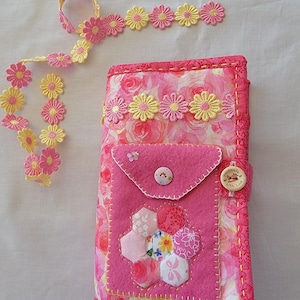 May include: A pink fabric journal cover with a floral print and a pink felt pocket. The pocket has a small pink button and a white button with the text "Handmade with Love". The journal cover is decorated with yellow and pink daisy trim.