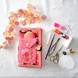 May include: A pink fabric sewing kit with a floral trim, a variety of sewing tools, and a small pocket on the front. The kit is open and the tools are visible.