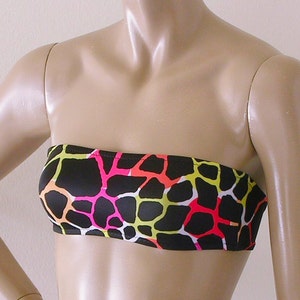 May include: A black strapless tube top with a colorful giraffe print. The print features neon pink, yellow, orange, and white irregular shapes against a black background. The top is displayed on a mannequin.