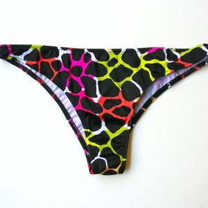 May include: A pair of black bikini bottoms with a vibrant pattern of irregular shapes in neon pink, yellow, and red, set against a black background. The bikini bottoms have a low-rise cut and a white interior lining.