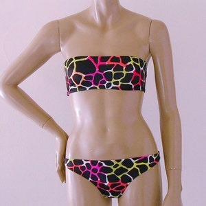 May include: A two-piece bikini set with a black background and a colorful giraffe print. The top is a strapless bandeau style, and the bottoms are a classic bikini cut. The print features pink, yellow, and orange shapes.
