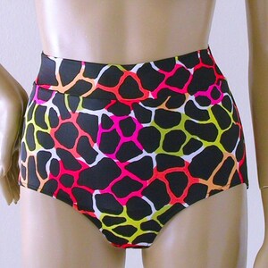 May include: High-waisted black shorts with a vibrant, colorful pattern. The design features a network of irregular shapes in neon pink, yellow, orange, and white, set against a black background. The shorts have a smooth, fitted appearance.