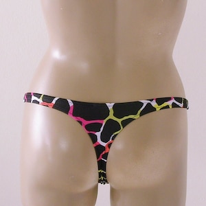May include: Black thong underwear with a colorful pattern of pink, yellow, and white shapes. The underwear is displayed on a mannequin, showcasing the back view of the garment.
