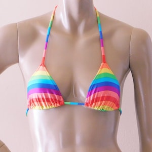 May include: A rainbow-striped bikini top. The triangle-shaped top features horizontal stripes in red, orange, yellow, green, blue, and purple. The straps and string are also rainbow-colored. The bikini top is displayed on a mannequin.