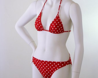 Puede incluir: Bikini rojo con lunares blancos. La parte superior es de estilo triangular con tirantes halter. La parte inferior a juego es de corte clásico. El traje de baño se exhibe en un maniquí blanco.