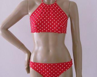 Puede incluir: Bikini de arriba y abajo de lunares rojos y blancos. La parte de arriba es de estilo halter con cuello alto. La parte de abajo es de estilo de corte alto.