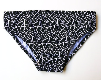 May include: Black and white patterned swim trunks with a geometric design.