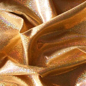 May include: Close-up of shimmering gold fabric with a textured, iridescent surface. The material is draped, creating folds and shadows that highlight its reflective qualities. The fabric has a metallic sheen.