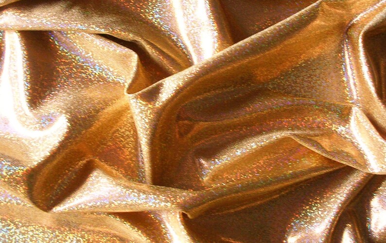 May include: Close-up of shimmering gold fabric with a textured, iridescent surface. The material is draped, creating folds and shadows that highlight its reflective qualities. The fabric has a metallic sheen.