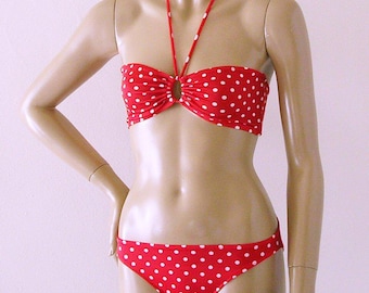 Puede incluir: Bikini de color rojo y blanco con lunares. La parte superior es de estilo halter con un detalle de anillo en el centro. La parte inferior es de corte clásico.