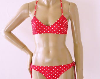 Puede incluir: Top y parte inferior de bikini de lunares rojos y blancos. La parte superior tiene la espalda cruzada y la parte inferior tiene lazos a los lados.