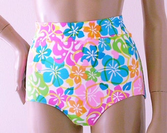 Pode incluir: Calcinha de fato de banho de cintura alta com um padrão floral vibrante. O design apresenta grandes flores de hibisco em tons de azul, rosa, laranja e amarelo sobre um fundo branco. A calcinha tem um corte alto na perna e uma cintura larga.