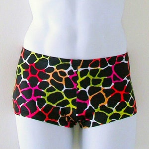 May include: Black and neon-colored boy shorts with a vibrant, abstract pattern. The shorts feature a repeating design of irregular shapes in neon pink, green, orange, and red, set against a black background. The garment is displayed on a white mannequin.