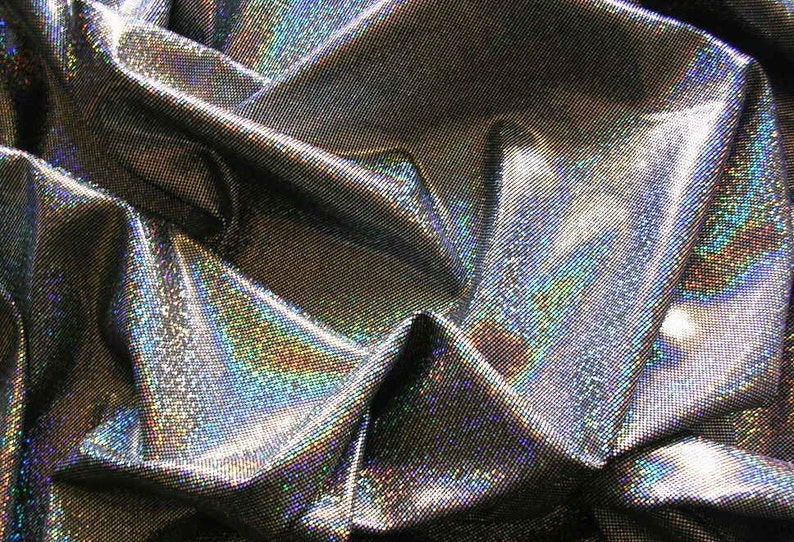 May include: Close-up of a shimmering, iridescent fabric with a metallic silver base. The fabric is heavily textured, with a subtle grid pattern. The folds and creases create highlights and shadows, enhancing the holographic effect. The fabric reflects a rainbow of colors.