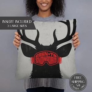 May include: A rectangular pillow with a black deer silhouette and the text "BORN TO SNOWBOARD" in red. The pillow has a light gray background and includes the text "INSERT INCLUDED 2 LARGE SIZES".