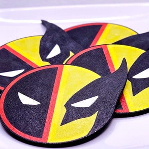 May include: Four round coasters with a black, red, and yellow design featuring a superhero character's mask.