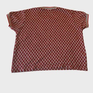 May include: A short-sleeved red and white patterned shirt. The shirt features a repeating pattern of red circles on a white background. The collar and sleeve edges have red, white, and black stripes.