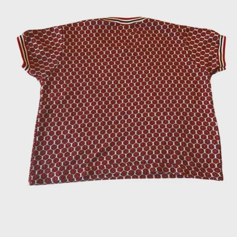 May include: A short-sleeved red and white patterned shirt. The shirt features a repeating pattern of red circles on a white background. The collar and sleeve edges have red, white, and black stripes.