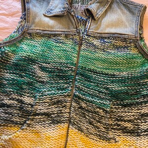 May include: A sleeveless denim vest with a knitted front. The vest features a light blue denim collar and shoulders, transitioning to a vibrant, striped knit in shades of green, yellow, and red. A full-length zipper runs down the front.