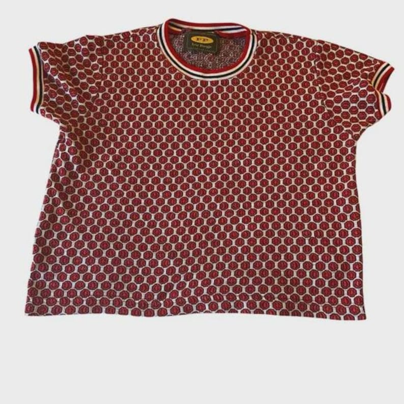 May include: Red and white short-sleeve t-shirt with a repeating pattern of red shapes. The shirt has a striped collar and sleeve cuffs. The tag on the collar reads "FP".