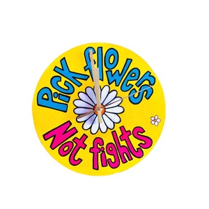 May include: A round, yellow clock with the words "Pick flowers Not fights" in blue and pink lettering. A white daisy is in the center, with clock hands pointing to the time. A small daisy is in the lower right corner.
