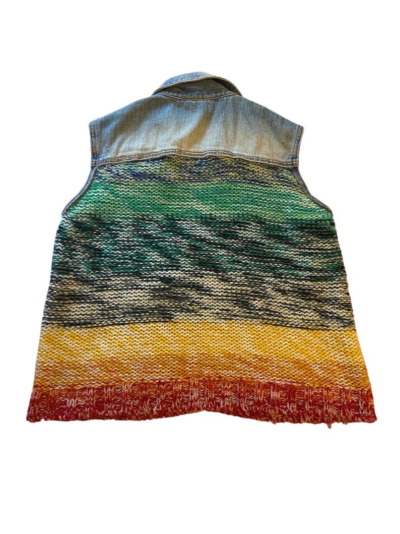 May include: A sleeveless vest with a denim upper and a knitted lower section. The knitted portion features horizontal stripes of green, black, yellow, and red. The vest has a collared neckline.