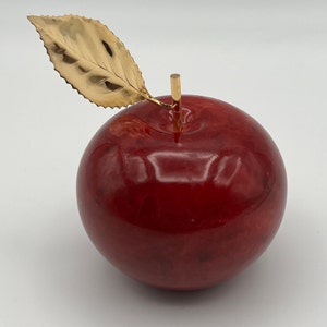 Könnte beinhalten: Dekorative Apfelskulptur mit poliertem, tiefrotem Körper und goldfarbenem Blatt und Stiel. Der Apfel ist eine realistische Darstellung der Frucht mit glänzendem Finish. Das Blatt hat detaillierte Adern.