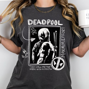 Könnte beinhalten: Ein dunkelgraues T-Shirt mit einer weißen Grafik von Deadpool. Die Grafik enthält den Text "Deadpool", "Maximum Effort" und "They call me the merc with a mouth".
