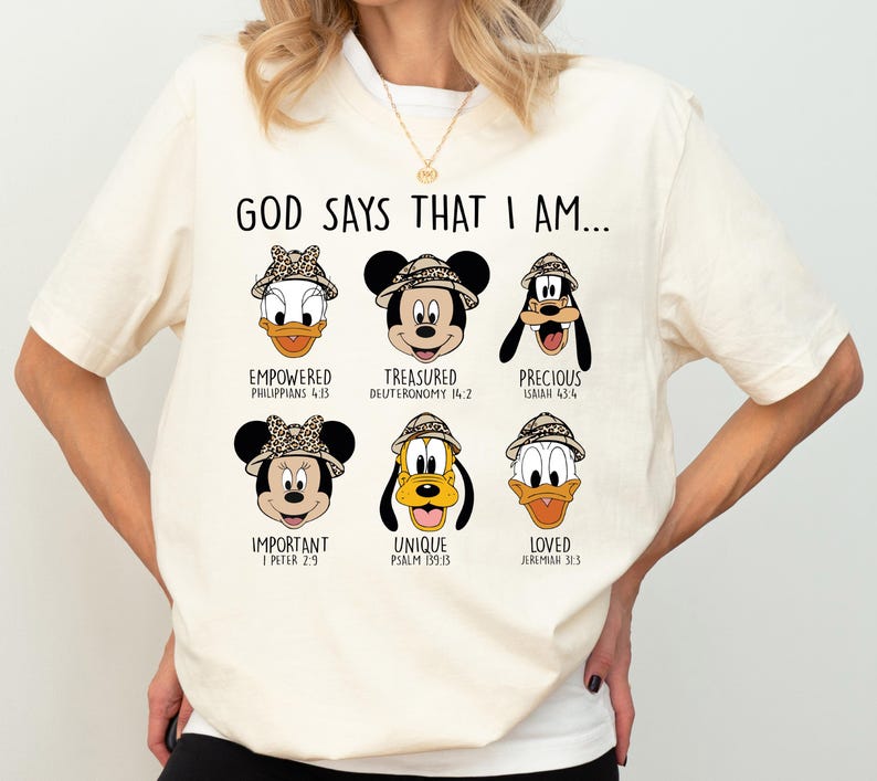 A white t-shirt with a graphic design featuring six cartoon faces of Disney characters, along with text that says "God says that I am..." and Bible verse references.