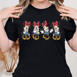 May include: Black t-shirt with a graphic of four Minnie Mouse characters in a row. Each Minnie Mouse is wearing a red bow and a blue and white polka dot dress.