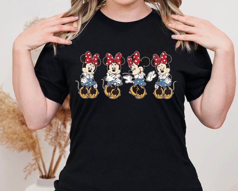 May include: Black t-shirt with a graphic of four Minnie Mouse characters in a row. Each Minnie Mouse is wearing a red bow and a blue and white polka dot dress.