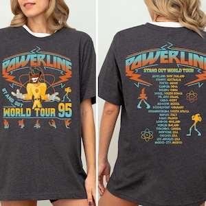 May include: A dark gray t-shirt with a graphic print of a cartoon character and the text "Powerline Stand Out World Tour 95". The back of the shirt lists a world tour schedule.